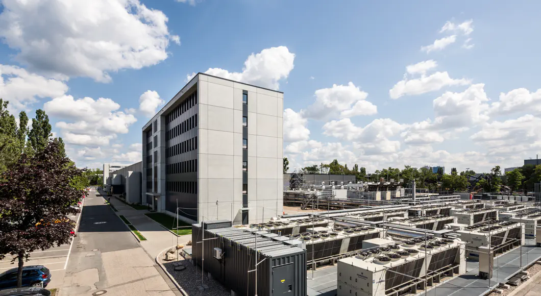 Industriegebäude, im Vordergrund Geräte, die aussehen wie Klimaanlagen. Blauer Himmel mit ein paar Wolken.