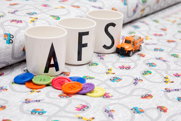 3 Tassen mit den Buchstaben A, F, S stehen auf Stoffballen, ein Spielzeugauto und bunte Knöpfe.